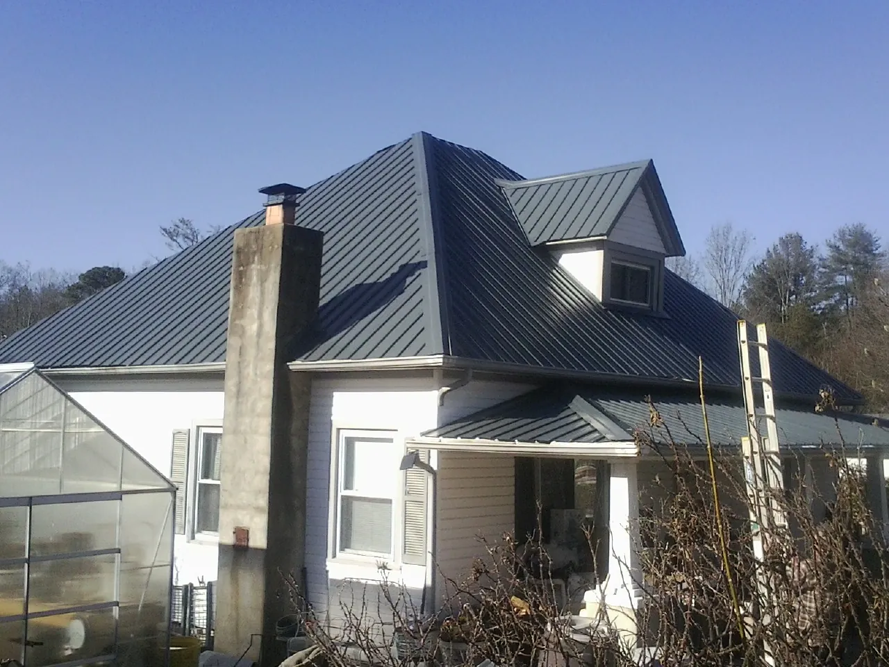 Dark blue standing seam metal roof on a white farmhouse with dormer — Slate & Tile Roof Repair by Roofing Brothers in Pledger