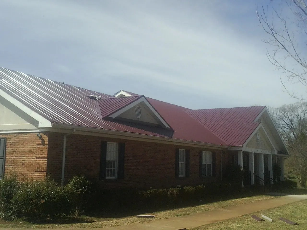 Red metal roof with gabled entries on a long brick building, from a Hail Damage Roof Repair job in Pledger