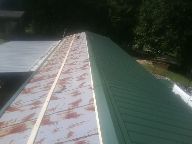 Old rusted panels beside newly installed green metal roofing — Wind Damage Roof Repair by Roofing Brothers in Pledger