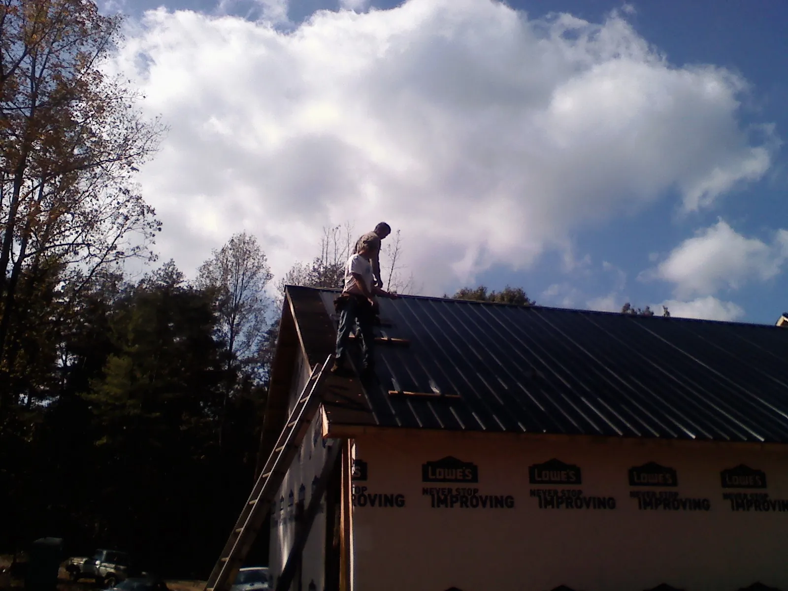 Roofer fastening dark metal panels high against a cloudy sky, from a Roof Inspection job in Pledger